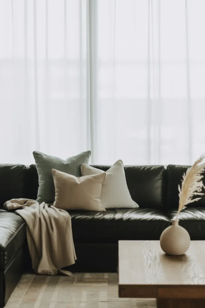 Black couch accented with soft sage green pillows in a calm room.