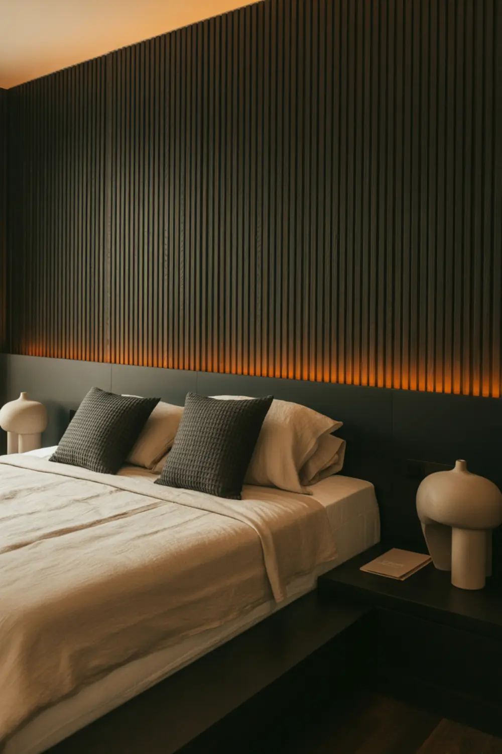 Modern black bedroom with vertical onyx slat wood paneling behind the bed and warm ambient lighting.
