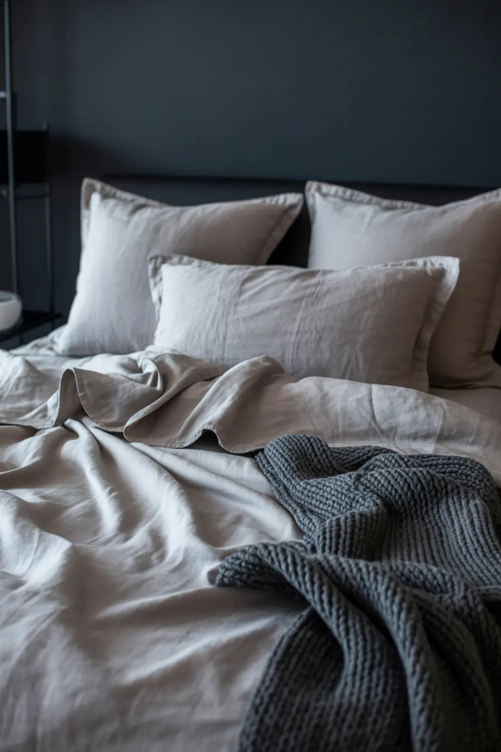 Ash-gray linen bedding paired with a chunky charcoal knit throw in a moody bedroom.